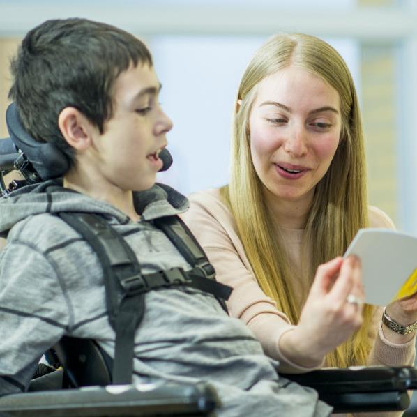 Une auxiliaire lit un livre à un enfant en situation de handicap moteur 