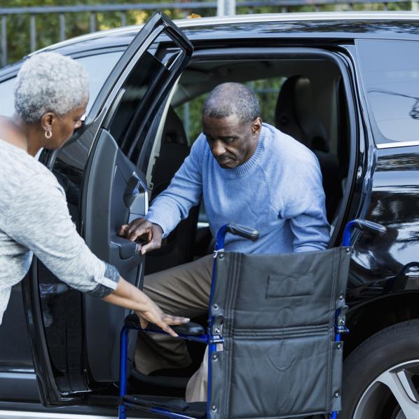 un homme handicapé sort d'une voiture pour s'installer dans son fauteuil roulant avec l'aide d'une femme
