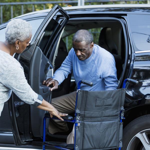 un homme handicapé sort d'une voiture pour s'installer dans son fauteuil roulant avec l'aide d'une femme