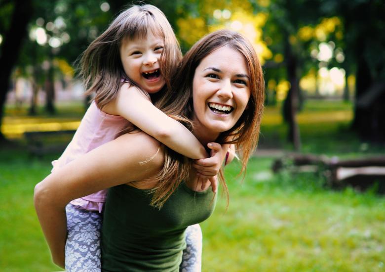 Une maman porte sa fille en situation de handicap sur son dos 