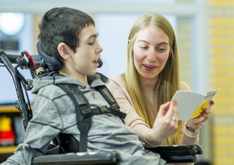 Une auxiliaire lit un livre à un enfant en situation de handicap moteur 